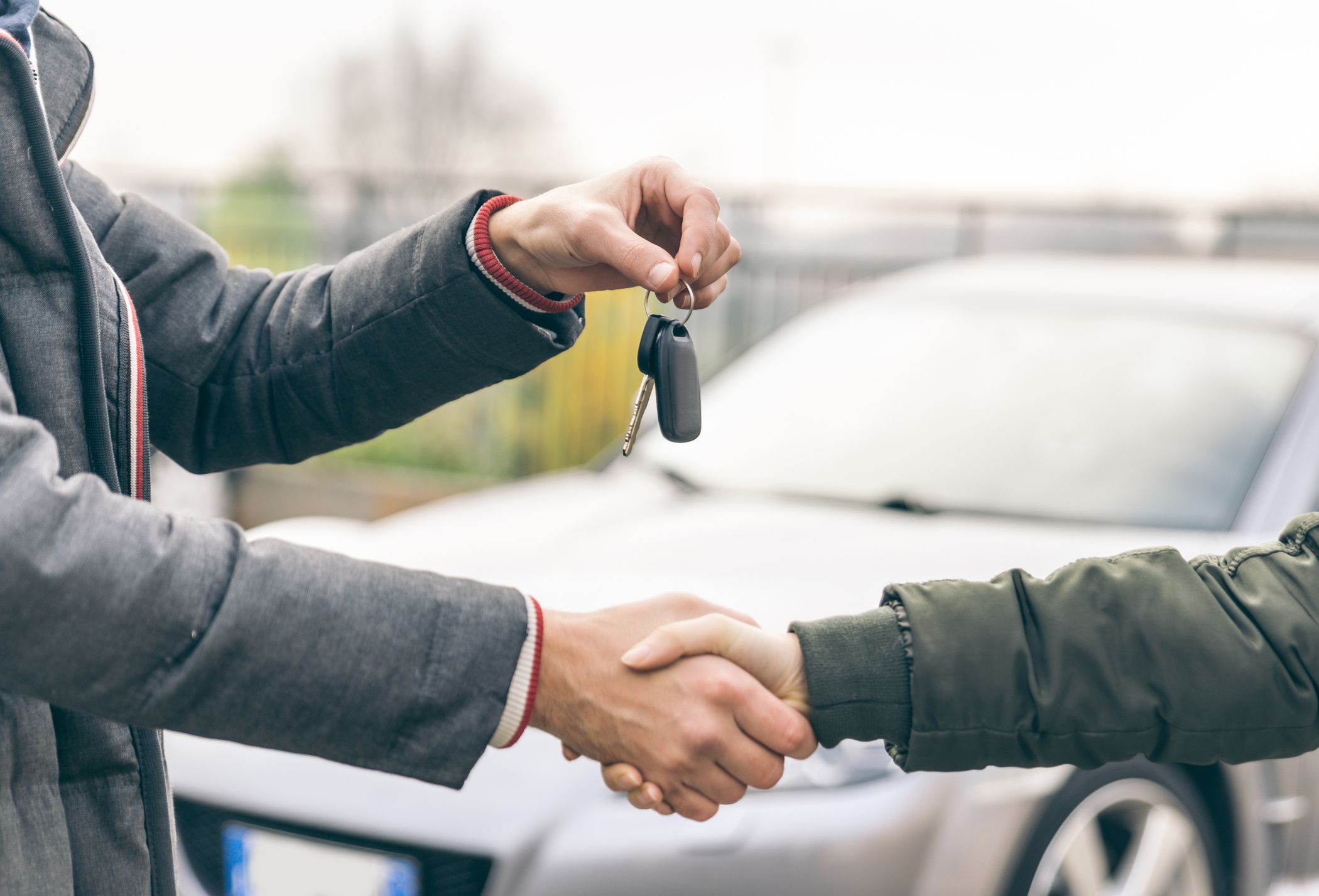 Dos personas dándose la mano mientras uno le entrega las llaves del auto al otro