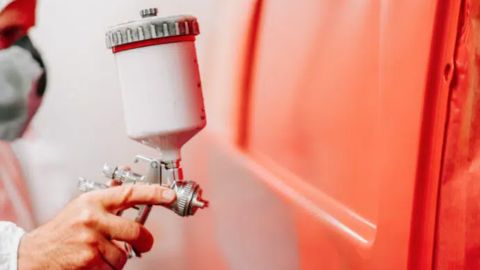 Técnico aplicando pintura roja a la carrocería de un vehículo en taller automotriz.