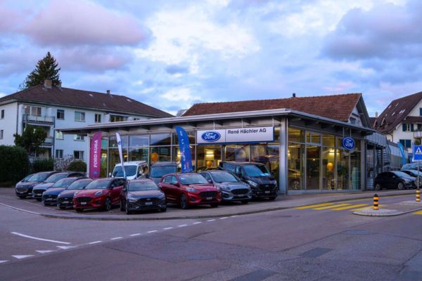Eingang der Garage René Hächler AG mit Lagerfahrzeugen auf Parkplatz fotografiert am Abend