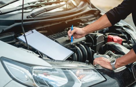 Ford Service Mechaniker inspiziert Motor und macht Notizen auf Clipboard