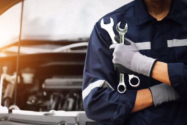 Automechaniker mit verschrönkten Händen hält Schraubenschlüssel in rechter Hand