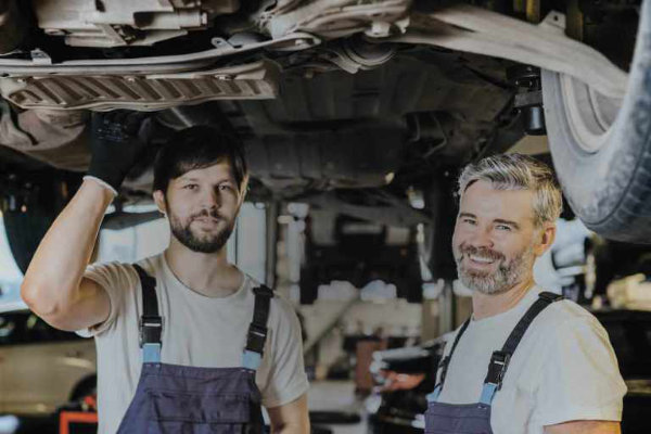 Zwei Mechaniker stehen unter Fahrzeug in Garage