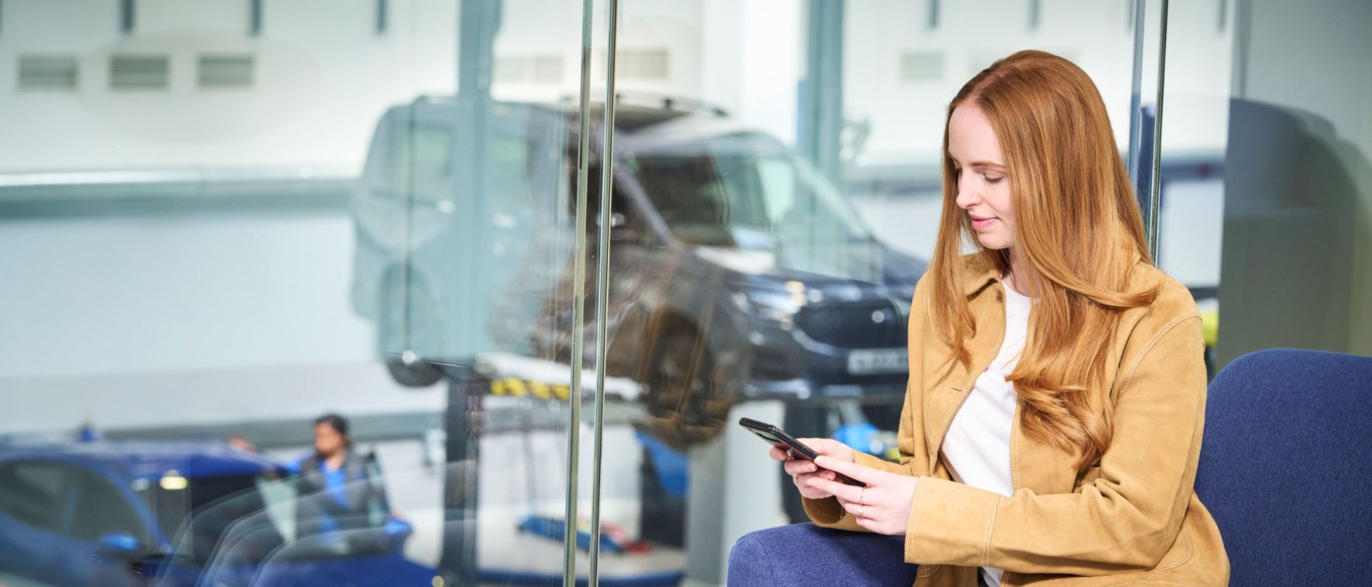 Frau blickt auf Handy während Ford Transit in Garage repariert wird