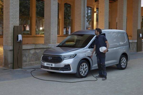 Elektromobilität Graues Ford Nutzfahrzeug parkt vor Gebäude und wird von Mann aufgeladen