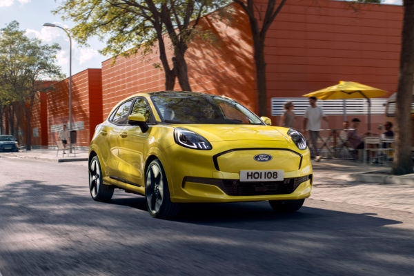 Ford Puma Gen-E La Ford Puma Gen-E traverse la ville en passant devant des personnes portant un parasol jaune