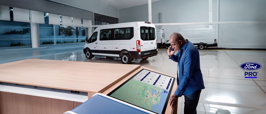 Ford Transit Minibus e Transit Furgão ao fundo, com homem falando ao celular e consultando tela grande com mapa