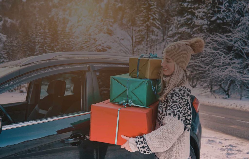 Frau mit drei grossen Weihnachtsgeschenken vor einem dunklen Ford Fahrzeug